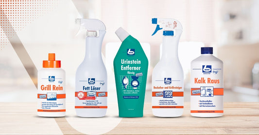 Eine Reihe von fünf Reinigungsprodukten auf einer Theke. Von links nach rechts: eine Flasche mit der Aufschrift „Grill Rein“, eine Flasche mit der Aufschrift „Fett Löser“, eine grüne Flasche mit der Aufschrift „Urinstein Entferner“, eine weiße Flasche mit blauer Düse mit der Aufschrift „Badreiniger und Grillreiniger“ und eine Flasche mit der Aufschrift „Kalk Raus“.