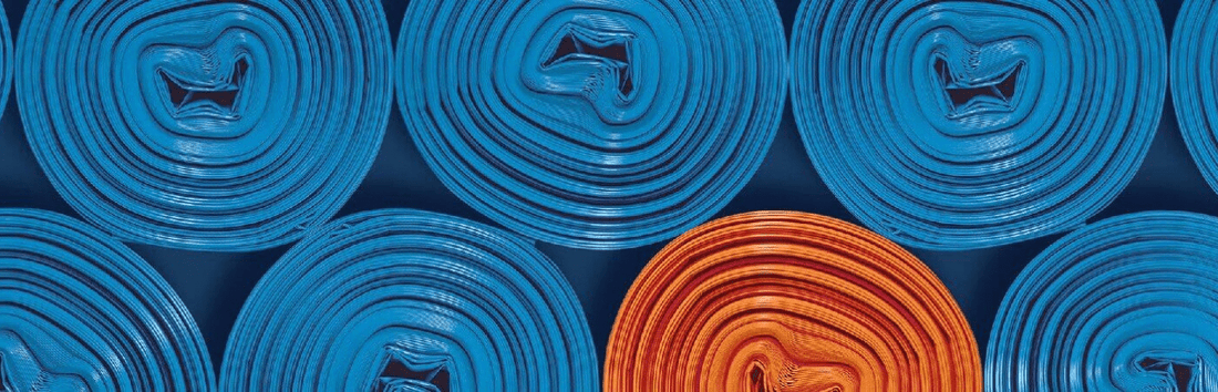 Mehrere aufgerollte blaue Matten von oben, eine orange Matte sticht farblich hervor, gleichmäßig angeordnet im Muster