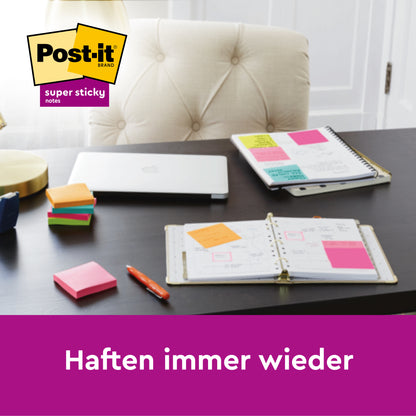 Ein Schreibtisch mit einem Laptop, zwei aufgeschlagene Planer mit bunten Post-it® Super Sticky Notes (76 mm x 127 mm, 90 Blatt/Block, 100% PEFC) der 3M Deutschland GmbH, Stapel von Post-it Blöcken, ein Stift und eine Lampe. Das Post-it-Logo und "Haften immer wieder" erscheinen.