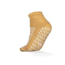 Abgebildet ist ein einzelner senfgelber ECO-PLUS Anti-Rutsch Einwegsocken beidseitig beschichtet von AMPri Handelsgesellschaft mbH auf weißem Hintergrund, mit weißen rutschfesten Griffen und ideal für medizinische Bereiche.