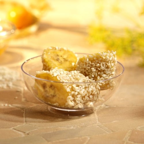 Drei Bananenstücke mit weißem Sesam werden in einer Starpak 50 Fingerfood-Schale (PS glasklar) serviert, platziert auf einer hellen Fliesenfläche mit sanft verschwommenem Hintergrund – ideal für Veranstaltungen.