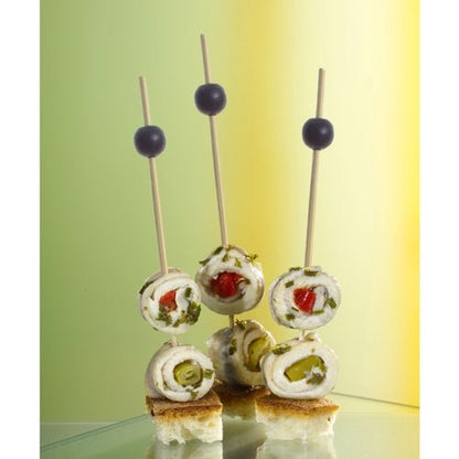 Three PAPSTAR 250 finger food picks from the PAPSTAR GmbH displays cheese, herb, and vegetable rolls on bread cubes, each garnished with a black olive. The softly lit background features shades of green and yellow.