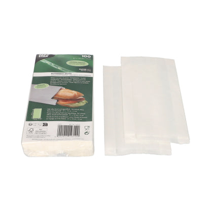 Ein Stapel weißer PAPSTAR Butterbrotbeutel fettdicht (21x10x3 cm) wird neben der grün-weißen Verpackung der PAPSTAR GmbH gezeigt, die ein Sandwich und eine Produktinformation zeigt. Neben der Packung (100 Stück) sind einige Schrumpffolienbeutel teilweise aufgefaltet.