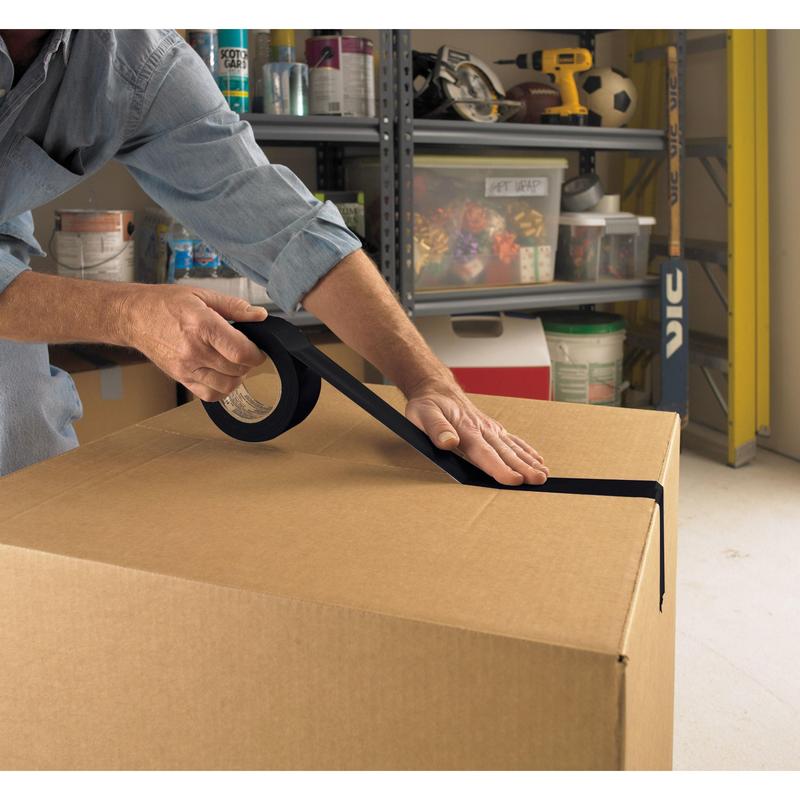 In einer Garage verschließt eine Person einen großen Karton mit Scotch® Universal Klebeband 2904 (50 m x 48 mm) der 3M Deutschland GmbH. In den Regalen dahinter lagern Gegenstände wie Farbdosen, eine Bohrmaschine und ein Fußball.