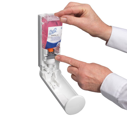 A person inserts a Scott® ESSENTIAL™ foam soap cartridge (pink, 200ml) from Kimberly-Clark GmbH into a wall dispenser and presses the orange part, while the open lid reveals the interior and the pink foam soap container.