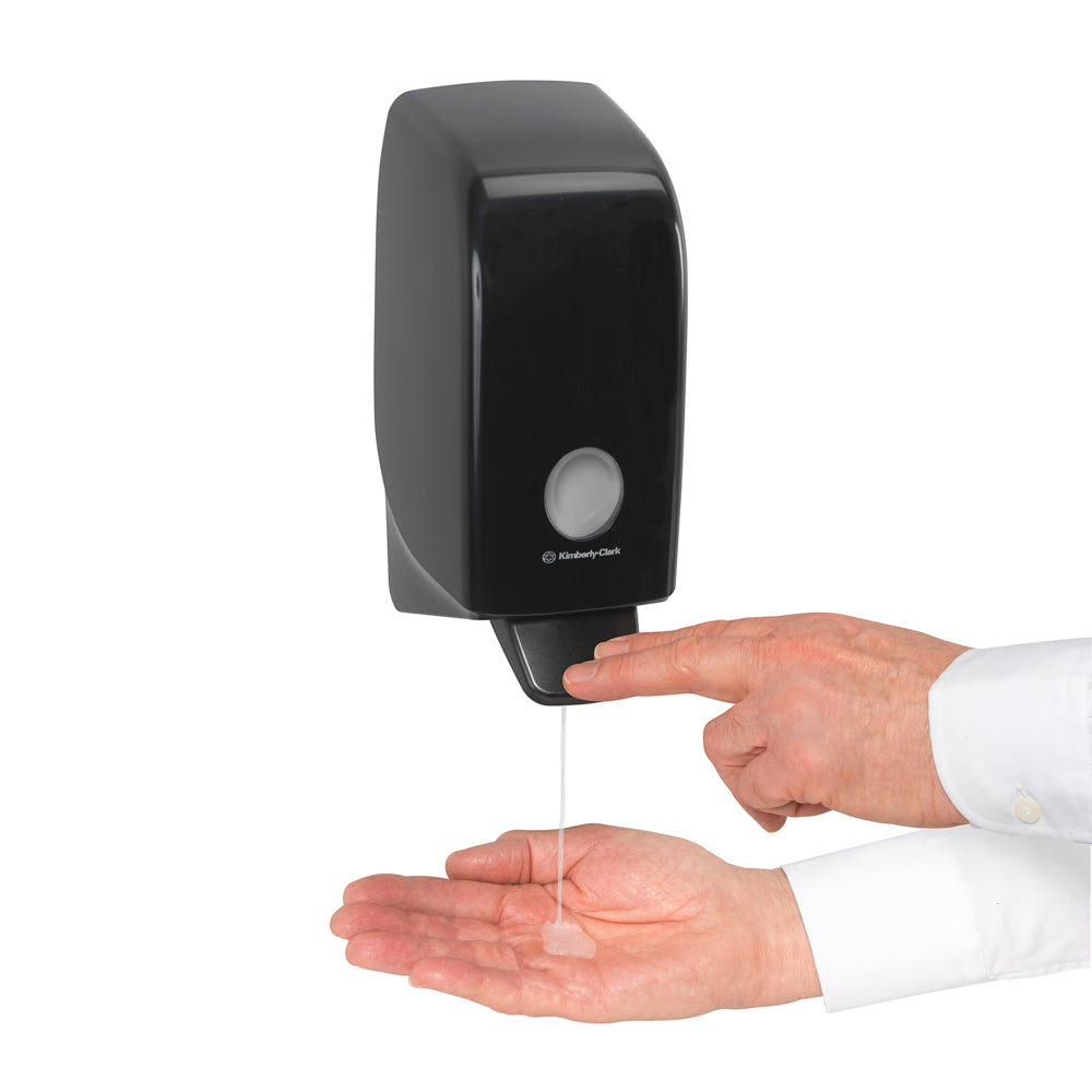 Jemand gibt Kleenex® Haar- und Körpershampoo von Kimberly-Clark GmbH aus einer weißen 1-Liter-Wandkassette in seine Handfläche und drückt den Hebel für eine effektive Reinigung und sanfte Pflege.