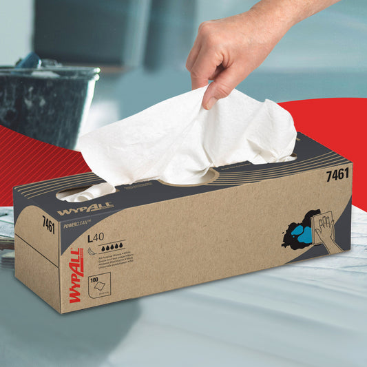 Eine Hand zieht ein weißes Blatt aus einer braunen WypAll® L40 PowerClean Zupfbox von Kimberly-Clark GmbH. Ideal für die industrielle Reinigung, zeigt die Box Produktinfos und ein Bild von Hochleistungs-Reinigungstüchern im Einsatz.