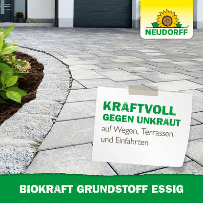 Eine gepflasterte Einfahrt neben einem gemulchten Gartenbeet mit Grünpflanzen. Ein Belag wirbt für BioKraft Grundstoff Essig von Neudorff Shop für unkrautfreie Terrassen, Wege und Einfahrten. Text: "KRAFTVOLL GEGEN UNKRAUT.
