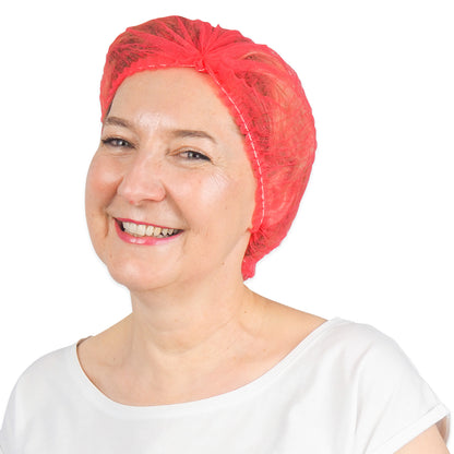 Eine lächelnde Frau in einem weißen Hemd und einer leuchtend roten ARNOMED COVER PP-KLIPPHAUBE Einmalklipphaube aus PP-Vlies (52 cm, ARNOWA GmbH) steht vor einem schlichten weißen Hintergrund.