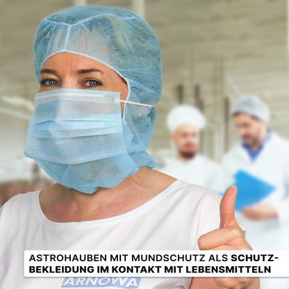 Eine Frau in Weiß, die den ARNOMED COVER PP-ASTROHAUBE MIT 2-LAGIGEM MUNDSCHUTZ der ARNOWA GmbH trägt, zeigt den Daumen nach oben; hinter ihr sind zwei Personen in weißen Uniformen unscharf zu erkennen. Der deutsche Text handelt von Schutzkleidung für den Kontakt mit Lebensmitteln.