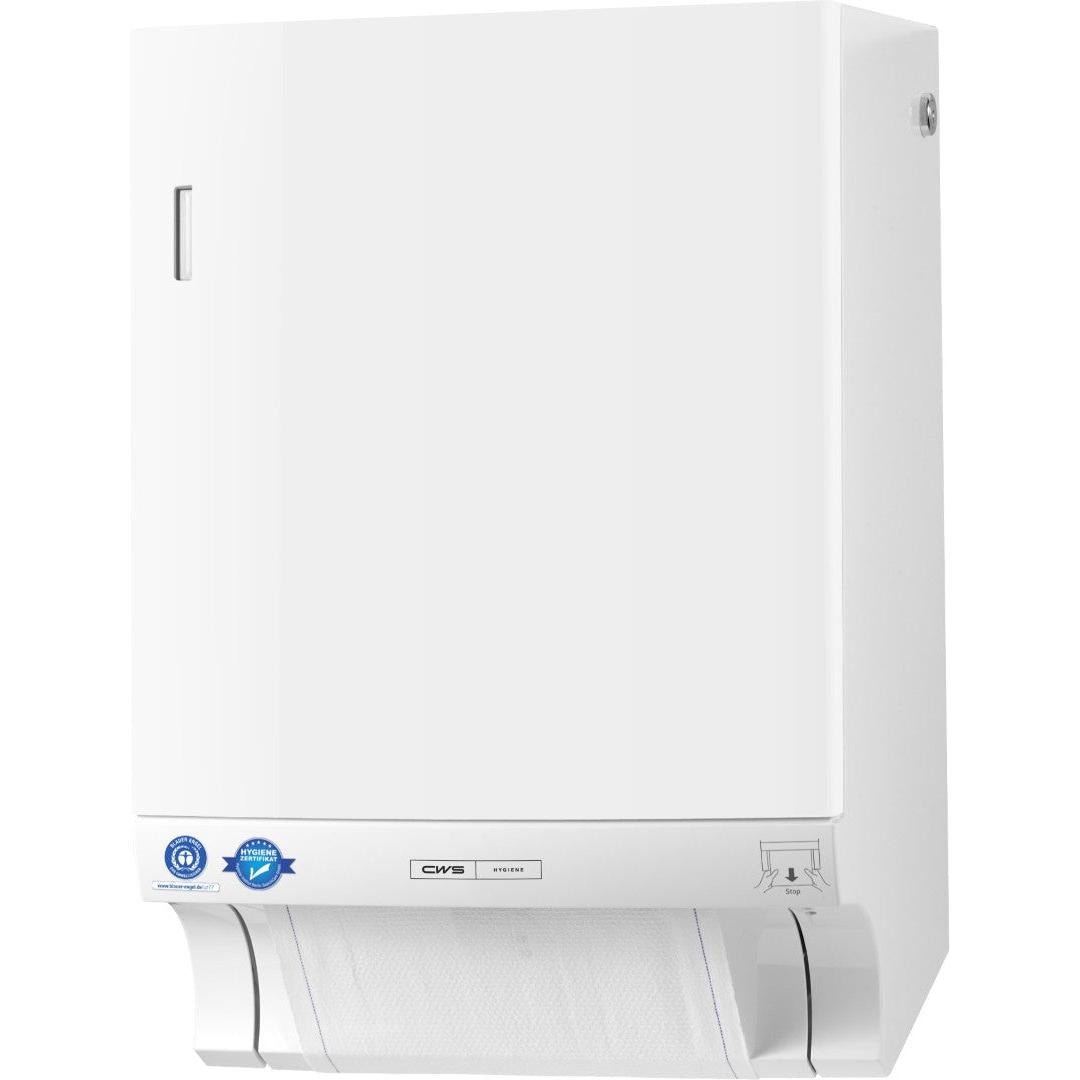 Ein weißer CWS ParadiseLine Stoffhandtuchspender Dry Slim inklusive Panel mit schlankem Design ist an der Wand befestigt und zeigt ein teilweise entnommenes Blatt am Boden. Blaue Aufkleber, ein kleines silbernes Etikett und eine illustrierte Anleitung befinden sich in der Nähe des Bodens.