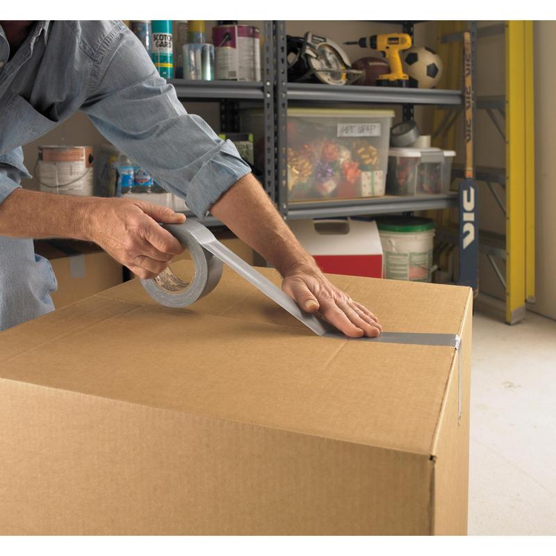 Eine Person verschließt einen großen Karton in einer Garage mit Scotch® Universal Klebeband 2904 (50 m x 48 mm) von 3M Deutschland GmbH, im Hintergrund sind Regale mit Werkzeug und Zubehör zu sehen.