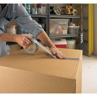 Eine Person verschließt einen großen Karton in einer Garage mit Scotch® Universal Klebeband 2904 (50 m x 48 mm) von 3M Deutschland GmbH, im Hintergrund sind Regale mit Werkzeug und Zubehör zu sehen.