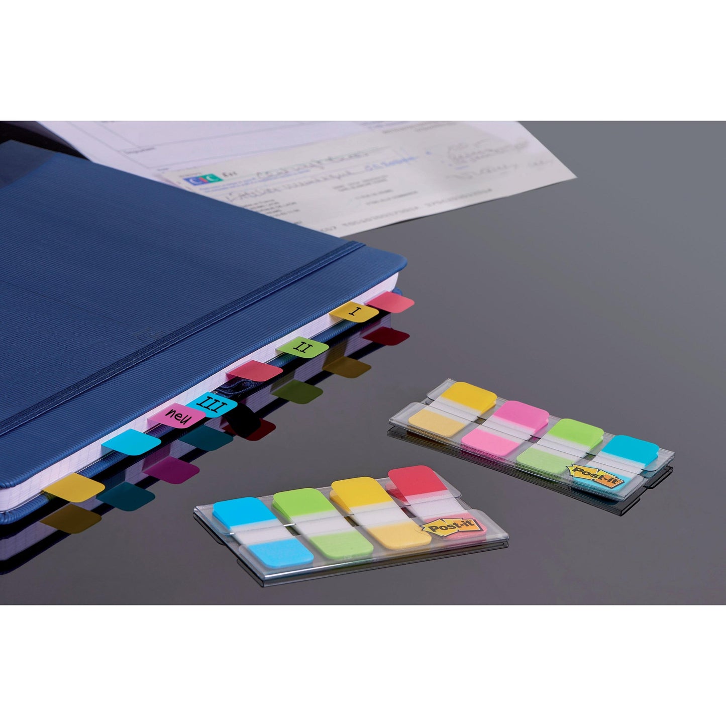 Ein blauer Ordner verwendet 3M Post-it® Index Strong Ablagetabs (Mini, Gelb, Rot, Blau, Grün), um die Abschnitte I-IV zu markieren. Zwei Packungen sortierter Haftstreifen in ihren Spendern liegen auf einer dunklen Fläche neben "Dokumente organisieren".