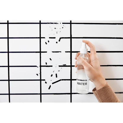 A hand holds a spray bottle labeled "WATER" in front of a Post-it® Easy Erase Whiteboard Surface, white from 3M Deutschland GmbH, which shows a black grid and some missing or erased lines.