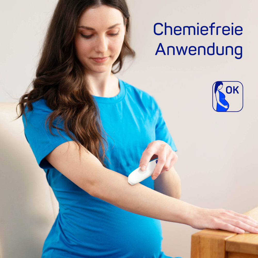 Eine schwangere Frau im blauen Shirt verwendet den HARTMANN Insektenstichheiler | Packung (1 Stück) der Paul Hartmann AG auf ihrem Arm, mit dem Text „chemiefreie Anwendung“ und einem Logo als Freigabesignal. Sie steht in einem sanft beleuchteten Raum.