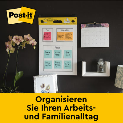 Eine Bürowand mit dem Post-it® Super Sticky selbsthaftendes Meeting Chart/Flipchart 559 von 3M Deutschland GmbH (63,5 x 76,2 cm), Monatskalender, Regal mit Glas, Orchidee und Fotos. Text: "Organisieren Sie Ihren Alltag.