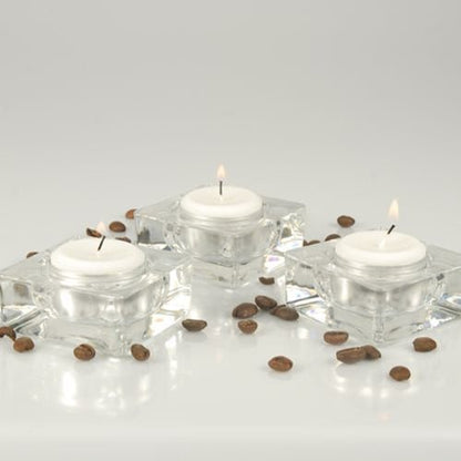 Drei Starpak Teelichter Ø 38 mm, weiß, mit 8 h Brenndauer aus der Faltschachtel (100 Stück) stehen in quadratischen Glasbehältern auf weißer Fläche mit verstreuten Kaffeebohnen vor hellem, schlichten Hintergrund.