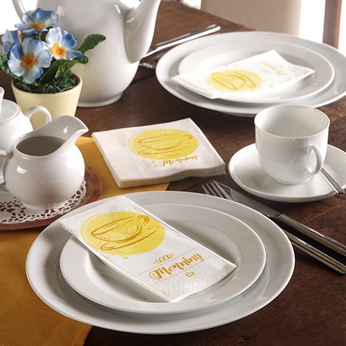Ein ordentlich gedeckter Tisch mit weißem Geschirr, einer Teekanne, blauen Blumen und 3-lagigen PAPSTAR-Servietten (33 x 33 cm) der PAPSTAR GmbH mit einer gelben Kaffeetasse und dem Schriftzug "Morning".