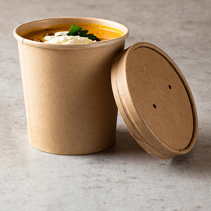 The Starpak 25 soup cup, round cardboard Ø 11.5 cm brown, is ideal for soup dishes on the go – here filled with orange soup, garnished with cream and parsley, on a gray surface with a matching lid.