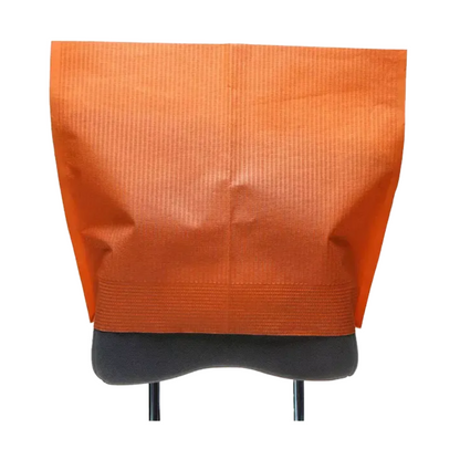 A headrest cover by AMPri Handelsgesellschaft mbH made of orange tissue paper fabric is elegantly draped over the backrest of a gray chair. Its textured surface enhances the design, with the chair legs partially visible underneath. The open top of the cover offers easy access and adds functional charm to this dental facility.