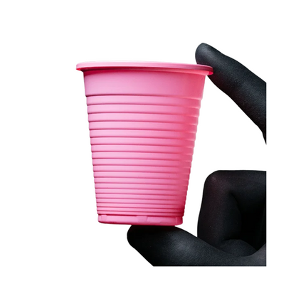 An elegantly gloved hand in black delicately holds a small, pink, ribbed AMPri Dental PP mouthwash cup from AMPri Handelsgesellschaft mbH against a flawlessly white background.