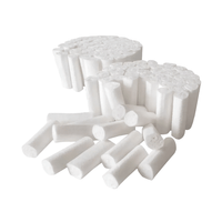 Two stacks of AMPri MED-COMFORT Dental cotton rolls—cylindrical in shape and white—are prominently displayed, with several scattered in the foreground. These disposable cotton rolls are manufactured by AMPri Handelsgesellschaft mbH from chlorine-free bleached cotton and are neatly arranged against a plain white background.