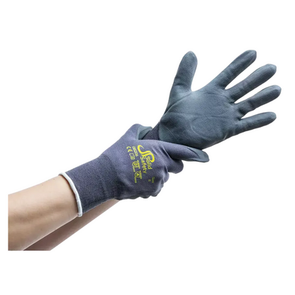 A person is wearing a dark blue, rubber-coated glove on the right hand and slipping into a matching glove on the left. These ultra-light assembly gloves AMPri SolidSafety Tough Micro Touch, available in sizes S to XXL and manufactured by AMPri Handelsgesellschaft mbH, are printed with yellow text and symbols on the back. The background is plain white.