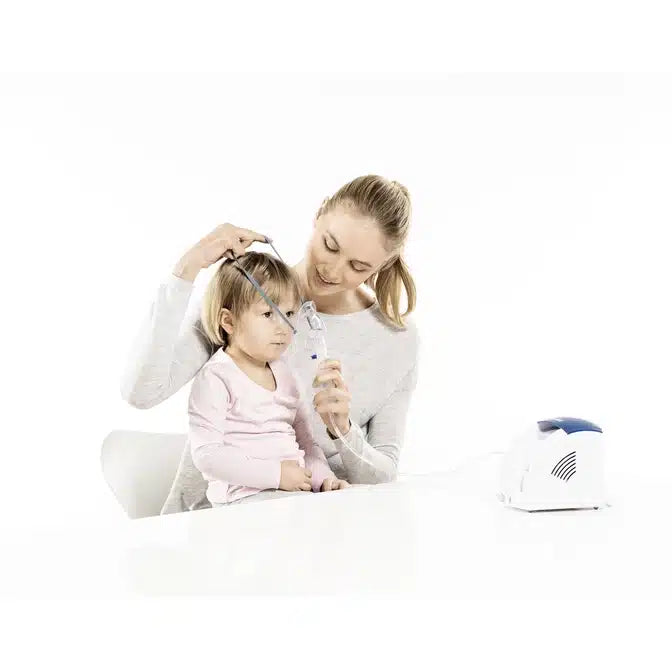Eine Frau hilft einem kleinen Kind bei einer Inhalationsbehandlung. Das in Rosa gekleidete Kind schaut aufmerksam zu, während die Frau eine Beurer Babymaske für verschiedene Inhalationsgeräte über das Gesicht des Kindes legt.
