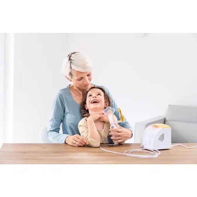 Eine Großmutter und ihre junge Enkelin lachen gemeinsam an einem Küchentisch, während sie mit einer Klebepistole basteln, in einem hellen und modernen Raum, der mit einem Beurer Inhalator IH 26 für Kinder zur Asthmalinderung ausgestattet ist.