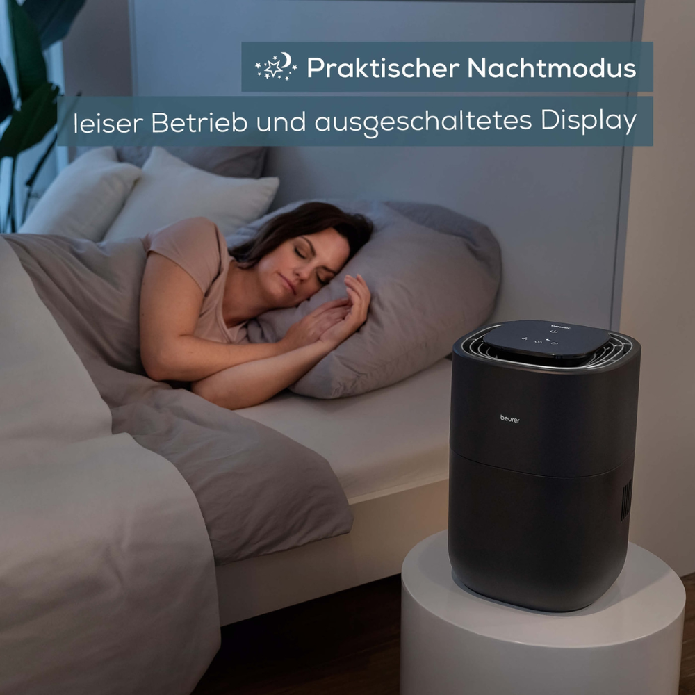 A woman sleeps in bed, next to her is a Beurer LB 200 humidifier with cold evaporation technology on the bedside table. The image is overlaid with a German text that reads: "Practical night mode, quiet operation, and display turned off." The room is dimly lit and the humidifier is active.
