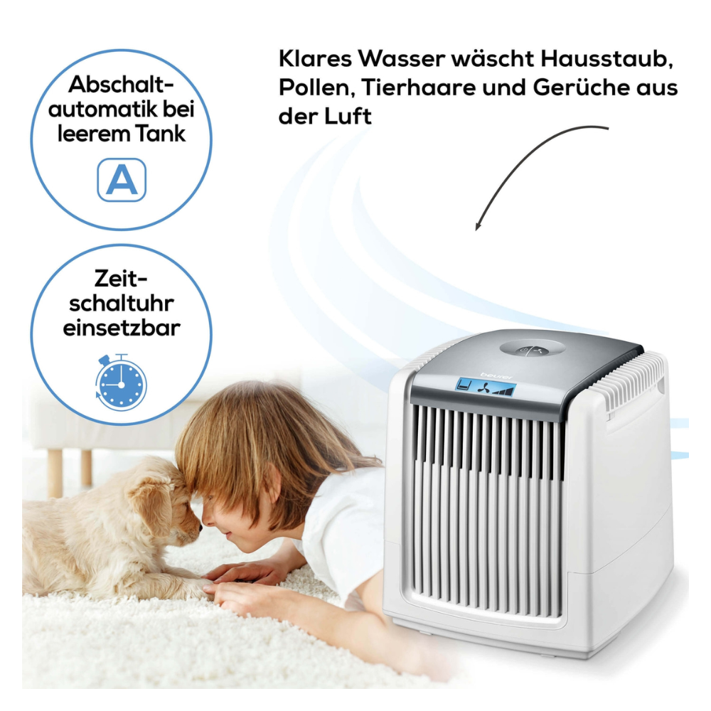 A child with blonde hair is lying on a carpet and attentively watching a small, white dog. Next to it is the Beurer air washer LW 230 White | Package (1 piece), an air purifier by Beurer GmbH with a digital display. The German text in the upper left corner highlights features such as automatic shut-off when the tank is empty and a timer.