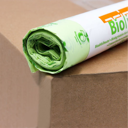 Eine Rolle grüner, biologisch abbaubarer DEISS Biomüllbeutel von Emil Deiss KG, teilweise ausgepackt und auf einer Kartonoberfläche liegend, zeigt das elementorientierte Verpackungsdesign.