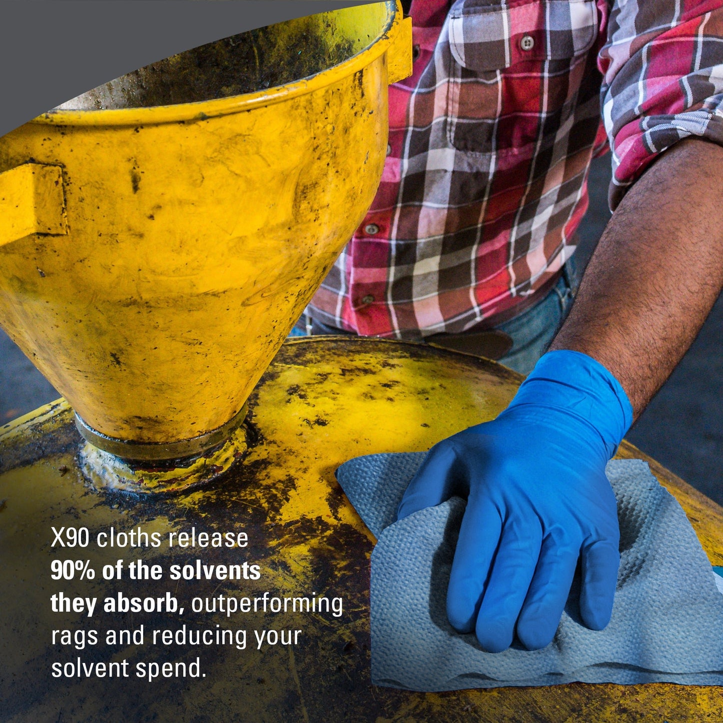 Eine Person mit einem blauen Handschuh wischt einen gelben Industrietank mit einem grauen Tuch ab. Der Text lautet: "WypAll® X90 PowerClean von Kimberly-Clark nimmt 90 % der Lösungsmittel auf und gibt sie wieder ab, was die Leistung von Putzlappen übertrifft und die Lösungsmittelkosten senkt.