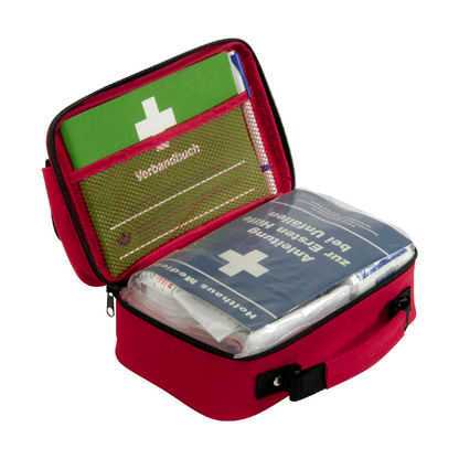 A compact red Holthaus first aid kit Office plus, DIN 13157 from Holthaus Medical GmbH & Co. KG, with a black handle that can be opened to reveal the contents. Inside are a green instruction manual and a blue Holthaus first aid bag decorated with a white cross and German text. The first aid equipment is neatly organized in mesh pockets and compartments, making it ideal for office environments.