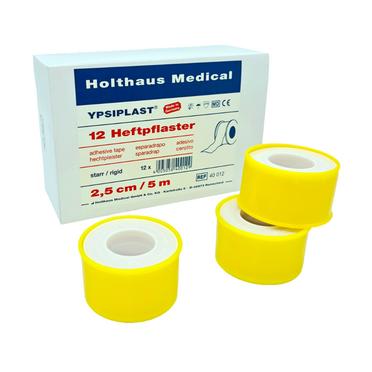 Eine Schachtel Holthaus Medical Ypsiplast® Heftpflaster und drei Rollen gelbes Klebeband sind vorn ausgestellt, jede Rolle ist 2,5 cm breit. Die Schachtel
