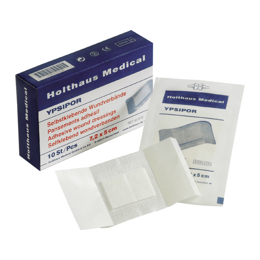 Eine Schachtel Holthaus Ypsipor Wundverband von Holthaus Medical, sterile Wundverbände, wobei ein Verband teilweise ausgepackt ist, so dass das Klebepad und die Schutzrückseite zu sehen sind.