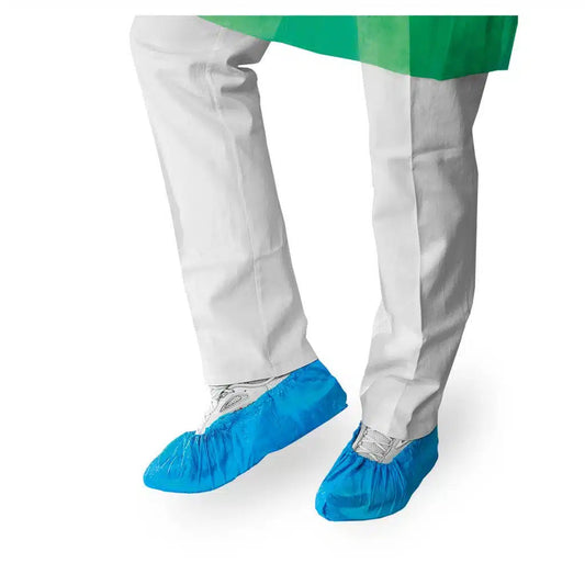 Eine Person in einem weißen Laborkittel und blauen Einweg-Schuhüberzügen der Meditrade GmbH steht vor einem weißen Hintergrund, wobei nur ihre Unterschenkel sichtbar sind.