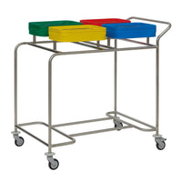 The Novocal "Kompakt plus" stainless steel four-bin laundry collector features a stainless steel frame, four wheels, a handle, and holds four colored bins (green, yellow, red, blue) for dirty laundry—each bin has a slot on top.