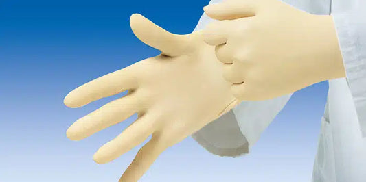 Eine Person im weißen Laborkittel zieht vor einem klaren blauen Hintergrund beige Hartmann Peha-soft® puderfreie Latex-Einmalhandschuhe an.