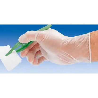 A person with a Hartmann Peha-soft® vinyl disposable glove, powder-free, holds a green plastic tweezer and clamps a piece of white gauze against the background of a blue sky.