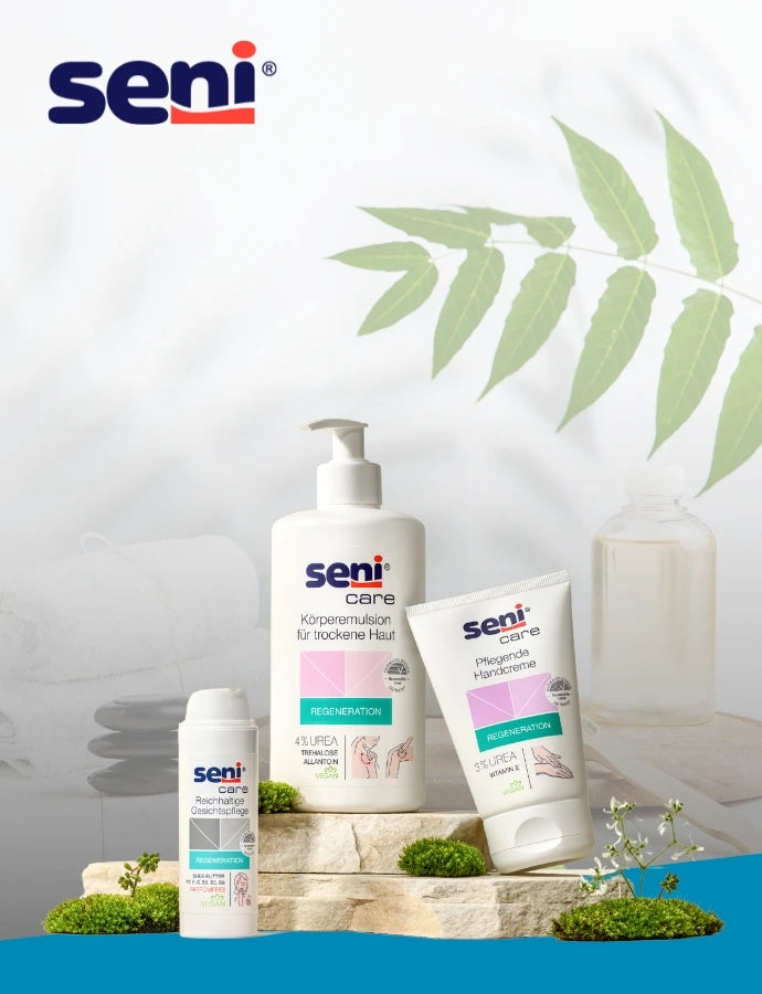 Seni Care Pflegeprodukte (Körperemulsion mit Pumpspender, Handcreme und Gesichtscreme) auf Naturstein-Podest arrangiert, mit grünem Moos dekoriert. Heller, minimalistischer Hintergrund mit Blatt-Schatten, gefalteten Handtüchern und Glasvase.