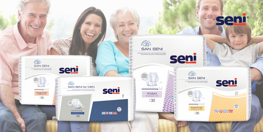Fünf Menschen, darunter drei Erwachsene und zwei Senioren, sitzen lächelnd zusammen. Im Vordergrund sind fünf Packungen mit Inkontinenzprodukten der Marke Seni in unterschiedlichen Sorten und Farben zu sehen, gekennzeichnet mit unterschiedlichen Saugstärken und Geschlechtsbezeichnungen.