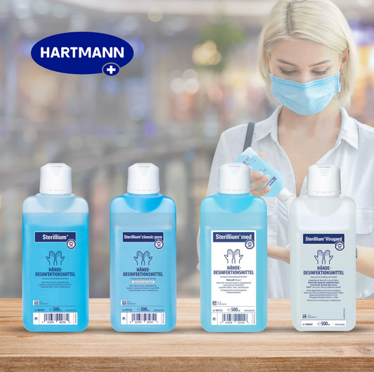 Das Bild zeigt eine Reihe von vier Flaschen mit Desinfektionsmittel der Marke Hartmann. Die Flaschen stehen auf einer Holzoberfläche, und im Hintergrund ist eine unscharfe Szene in einem Innenraum zu sehen. Eine blonde Frau trägt eine medizinische Maske und ein weißes Hemd und hält eine weitere Flasche Desinfektionsmittel in der Hand. Oben links im Bild befindet sich das Hartmann-Logo.
