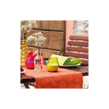 A wooden table is adorned with a bright red-orange PAPSTAR table runner fabric-like PV-Tissue Mix from the ROYAL Collection of PAPSTAR GmbH. It is decorated with colorful vases – red, pink, yellow, and orange – some containing white flowers. Green leaves are artfully placed beside the vases. Wooden chairs surround the elegant arrangement.