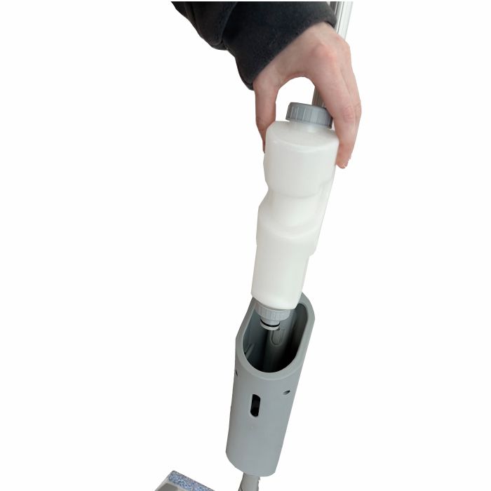 A person inserts a white cleaning solution bottle into the handle of the Arcora Ultra Mobile Spray Mop System by Arcora International GmbH on a white background.