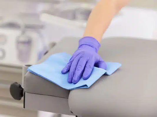 Eine Person mit violetten Handschuhen reinigt in einer Klinik- oder Laborumgebung eine graue Oberfläche mit einem Vileda r-MicronQuick Microfasertuch - 5 Tücher.