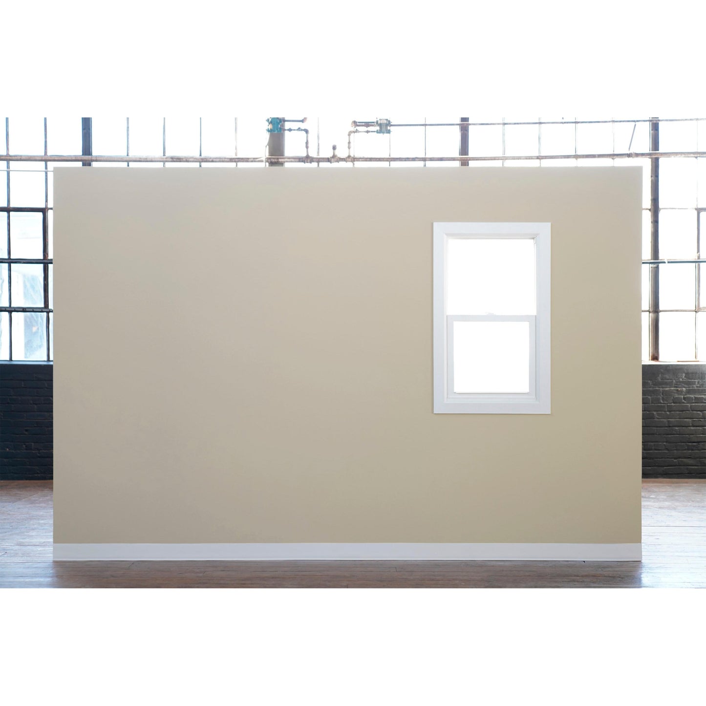 Eine beige Wand mit einem weiß gerahmten Fenster steht vor großen Industriefenstern - ideal zum Streichen mit Scotch® Classic Abdeckband, 24 mm x 50 m, von 3M Deutschland GmbH (70% PEFC, SGSCH-COC-110078) - in einem großen Raum mit Holzboden.