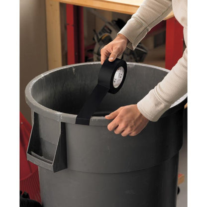 Eine Person klebt Scotch® Universal Klebeband 2904 (50 m x 48 mm) von 3M Deutschland GmbH auf den Rand eines großen grauen Abfalleimers in einer Werkstatt, mit einer Werkbank und Werkzeugen im Hintergrund.