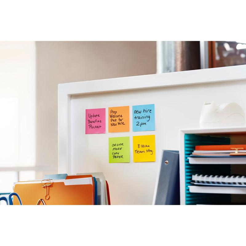 Four Post-it® Super Sticky Notes (76x76 mm, 90 sheets/block, 100% PEFC) from 3M Deutschland GmbH display handwritten reminders - achievements, training, paper order, team meeting - on a white office partition, with folders and accessories nearby.